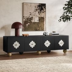 a black and white sideboard with three flowers on it in front of a painting