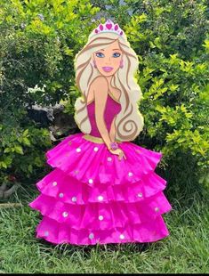 a cardboard barbie doll sitting on top of a lush green grass covered field with trees in the background