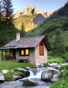 a small cabin sits next to a stream in the mountains