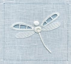 a white dragonfly on a light blue linen fabric background with stitchs and beads