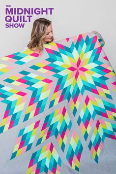 a woman holding up a colorful quilt with the words midnight quilt show written on it