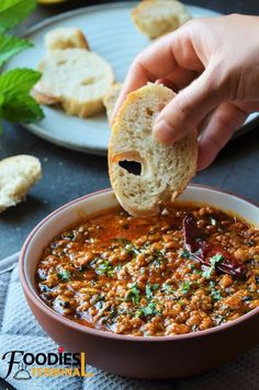 a person dipping some bread into a bowl of soup with other food on the side