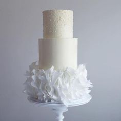 a three tiered white wedding cake with ruffles