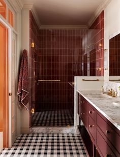 a bathroom with black and white checkered floor, red cabinetry, and gold fixtures