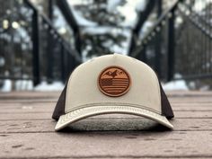 Elevate your style with our unique Mountain Flag leather patch hat, featuring a stunning design that combines mountains and the American flag. The Mountain Flag design is perfect for outdoor enthusiasts and patriots alike, adding a touch of rugged charm to your look. Available on the Richardson 112 FP, a five-panel hat that features a seamless design without a seam down the center of the face, this hat offers a comfortable and stylish fit. The Mountain Flag design is available in multiple colors Western Style Baseball Cap With Flat Bill For Outdoor, Brown Trucker Hat With Logo Patch For Outdoor, Western Style Baseball Cap With Curved Brim For Outdoor, Western Style Brown Trucker Hat For Outdoor, Brown Flat Bill Snapback Hat For Hiking, Western Trucker Hat With Leather Patch For Outdoor, Brown Curved Bill Baseball Cap For Outdoor Activities, Brown Trucker Hat For Outdoor Activities, Country Style Brown Baseball Cap For Outdoor