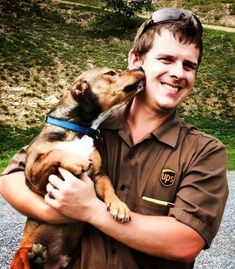 a man holding a dog in his arms and smiling at the camera with grass behind him