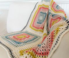 a crocheted blanket is sitting on a white couch next to a pillow and pillows