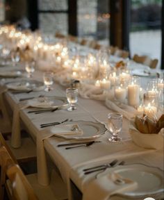 a long table is set with white plates and silverware, lit by candlelight