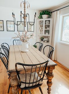 a dining room table with chairs and a vase on top of it in front of a window