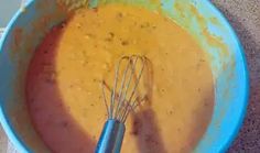 a blue bowl filled with yellow liquid next to a whisk