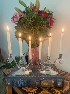 a table topped with a book and lit candles next to a vase filled with flowers