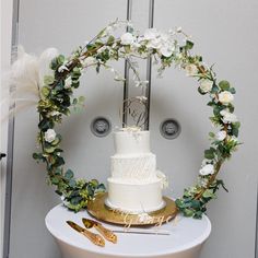 a white wedding cake sitting on top of a table with greenery and flowers around it