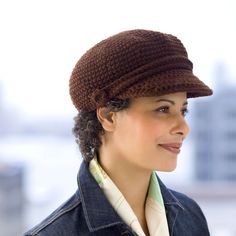 a woman wearing a brown crochet hat and denim jacket in front of a cityscape