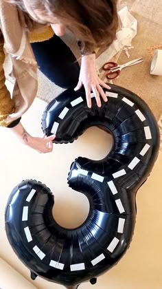 a woman is holding two large black balloons that spell out the number three, with her hands