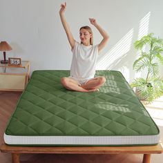 a woman sitting on top of a green mattress with her arms up in the air