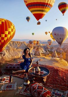 a woman sitting on top of a rug with hot air balloons in the sky above