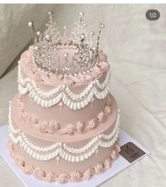 a three tiered cake with pink frosting and a tiara on the top