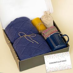 an open box containing coffee mugs, socks and a note with congratulations written on it