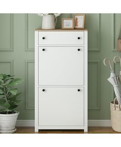 a white cabinet sitting next to a potted plant