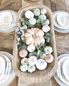 a wooden tray filled with white pumpkins and greenery on top of a table