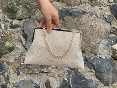 a person holding onto a white purse in front of a rock wall