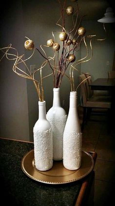 three white vases with branches in them on a table