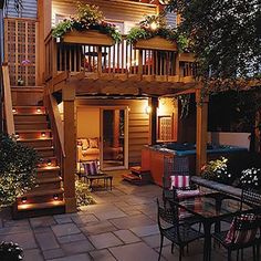 an outdoor patio with stairs, table and chairs at night in front of a house