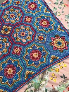 a colorful crocheted blanket on top of a bed covered in flowers and leaves