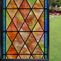 a stained glass window in the middle of a grassy area with trees and flowers behind it