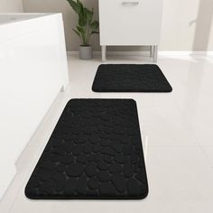 two black bath mats sitting on top of a bathroom floor next to a white cabinet