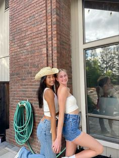 two women standing next to each other in front of a brick building with a cowboy hat on