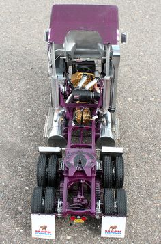 a purple toy tractor with two large tires on it's flatbed, parked in a parking lot