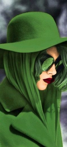 a woman with green hair wearing a green coat and hat, holding her face covered by a veil