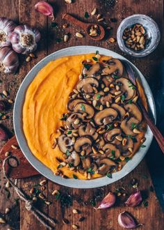 a bowl filled with carrot hummus next to some garlic and other ingredients on a wooden table