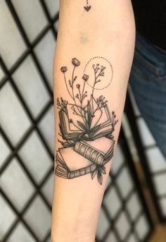 a woman's arm with a book and flowers tattoo on the left inner forearm