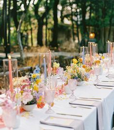 a long table with flowers and candles is set up for an outdoor wedding reception in the woods