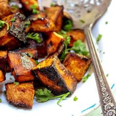 a white plate topped with fried tofu and parsley next to a silver fork