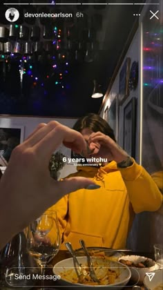 a woman in a yellow jacket is eating food at a table with two hands on her face