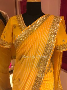 This is a pretty Gota Danka Handwork Yellow Leheriya Saree is a hand tie and dye saree with fine white lines. The beautiful leheriya saree has gota and danka work in gold color and looks very beautiful. The saree has fine hand work on blouse. Throughout the saree, there are delicate flower motifs in both gota and danka work. The blouse matching the saree makes the saree look even prettier. Leheriya is a traditional Rajasthani style of bandhani tie and dye. Product Highlights Gota Danka Handwork Yellow Leheriya Saree: Fabric Type: Pure georgette and pure crepe Embroidery: Gota patti and Danka work Color: Yellow. Free Service: This Gota Danka Handwork Yellow Leheriya Saree is sent well finished with edge and back finishing. The saree is also roll pressed before it is sent. The saree has latk Yellow Bandhani Dress, Hand Work On Blouse, Danka Work, Lehariya Saree, Tie And Dye Saree, Lehriya Saree, Work On Blouse, Leheriya Saree, Haldi Wear