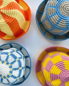 four crocheted baskets sitting next to each other on a white surface with different colors