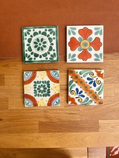 four colorful tiles are arranged on a wooden table in the shape of square flowers and leaves