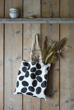 a black and white polka dot tote bag hanging on a wooden wall next to a plant