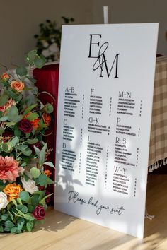 a wedding seating chart with flowers and greenery next to it on a wooden table