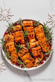 salmon with rosemary and pomegranate on a white platter surrounded by snowflakes