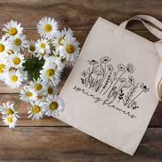 Welcome spring with this attractive yet functional canvas tote bag. Featuring some beautiful wildflowers with the phrase "Spring Flowers" in an eye-catching script font, this sustainable tote bag would make the perfect birthday or Mother's Day gift.   This 100% cotton bag comes in one size - 15" x 16"- perfect for everyday use. The heavy canvas fabric is durable and will last for years. This functional bag features 20" canvas handles, allowing you to carry lots of flowers or farmer's market trea White Canvas Bag For Spring, Eco-friendly Spring Canvas Bag For Everyday Use, White Botanical Style Bag For Spring, Eco-friendly Flower Shaped Bags For Spring, Eco-friendly Canvas Bag For Everyday Spring Use, Eco-friendly Flower-shaped Bags For Spring, Spring Botanical Rectangular Bags, Spring Canvas Tote Bag As Gift, Spring Cotton Bags With Letter Print