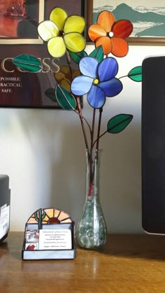 a glass vase with colorful flowers in it on a desk next to a computer monitor