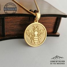 a gold pendant with a bee on it sitting on top of a wooden box next to a