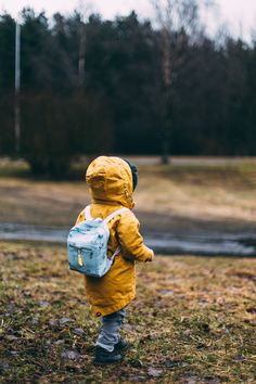 a small child wearing a yellow raincoat and carrying a blue backpack with the words never to early to start your journey