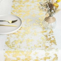 a white table topped with a plate covered in yellow flowers and gold leafy napkins