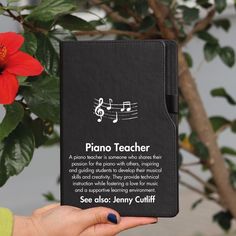 a person holding up a black book with music notes on it and a red flower in the background